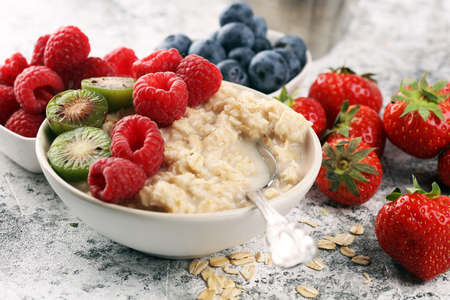 Bowl of oatmeal porridge with banana, raspberries, blueberries coconut and caramel sauce on rustic table, hot and healthy food for Breakfast.の写真素材