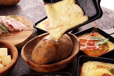 Delicious traditional Swiss melted raclette cheese on diced boiled or baked potato served in individual skillets with salami and potatoesの写真素材