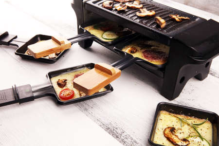 Delicious traditional Swiss melted raclette cheese on diced boiled or baked potato served in individual skillets with salami and potatoesの写真素材