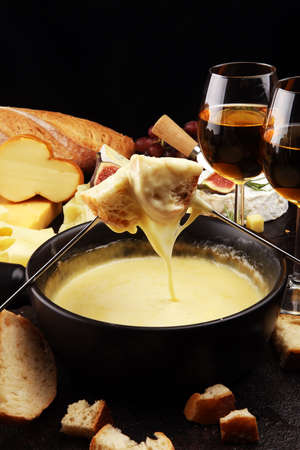 Gourmet Swiss fondue dinner on a winter evening with assorted cheeses on a board alongside a heated pot of cheese fondue with two forks dipping bread の写真素材