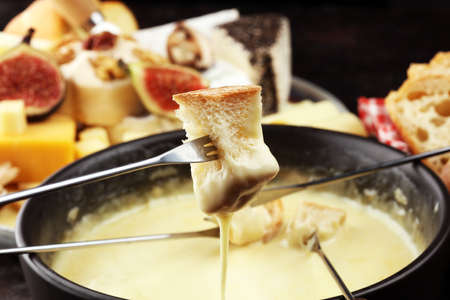 Gourmet Swiss fondue dinner on a winter evening with assorted cheeses on a board alongside a heated pot of cheese fondue with two forks dipping bread の写真素材