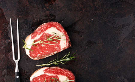 Raw fresh meat Ribeye Steak, seasoning and meat fork on a tableの写真素材