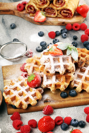 Traditional belgian waffles with fresh blueberries, sugar and raspberries on wood