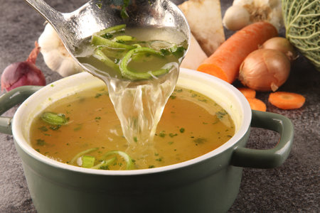 Broth with carrots, onions various fresh vegetables in a pot - colorful fresh clear spring soup....