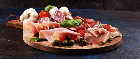 Food tray with delicious salami, pieces of sliced prosciutto crudo, sausage and basil. Meat platter...