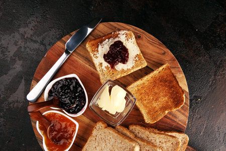 Toast bread with homemade strawberry jam and apricot marmalade on rustic table served with butter...