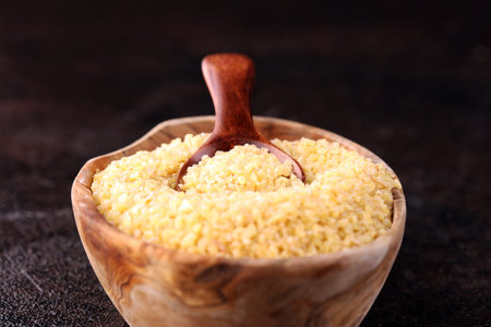 Uncooked bulgur in wooden spoon, rustic style. Bulgur wheat grains. healthy food