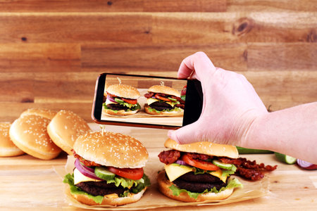 takes a picture smartphone eating fast food. Delicious homemade burgers. Tasty fresh meat burgers...