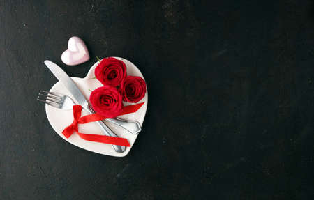 Red rose on white dish. Meal on Valentines Day. Valentines day table setting with plate, knife, fork, ribbon and hearts. Holidays background. Valentines day backgroundの写真素材