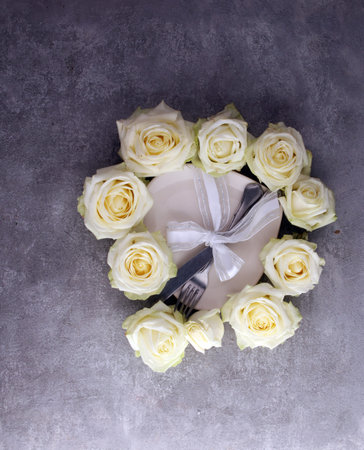 white rose on white dish. Meal on Valentines Day. Valentines day table setting with plate, knife,...