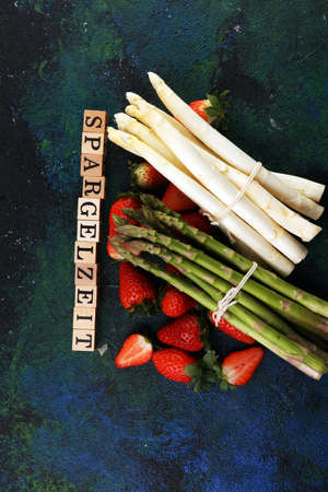 White and green fresh asparagus with a bunch of healthy strawberries with Spargelzeit wooden letter.の写真素材