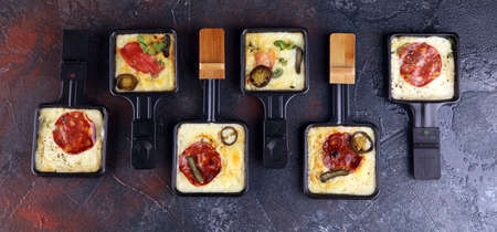 Delicious traditional Swiss melted raclette cheese on diced boiled or baked potato served in individual skillets with salami and potatoesの写真素材