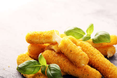 Breaded mozzarella cheese sticks with basil on tableの写真素材