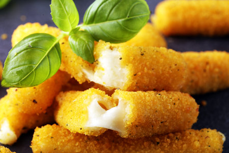 Breaded mozzarella cheese sticks with basil on table