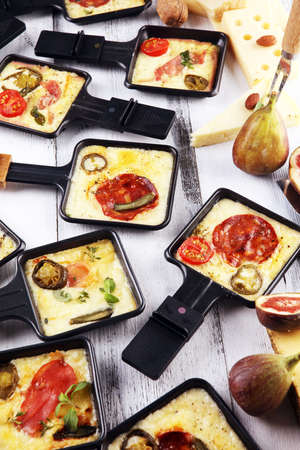 Delicious traditional Swiss melted raclette cheese on diced boiled or baked potato served in individual skillets with salami and potatoesの写真素材