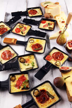 Delicious traditional Swiss melted raclette cheese on diced boiled or baked potato served in individual skillets with salami and potatoesの写真素材