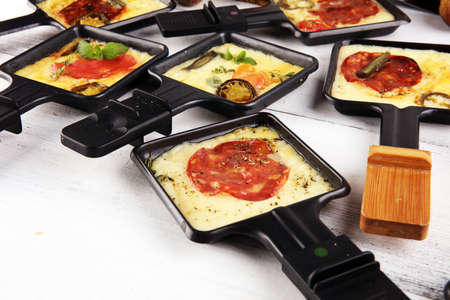 Delicious traditional Swiss melted raclette cheese on diced boiled or baked potato served in individual skillets with salami and potatoesの写真素材