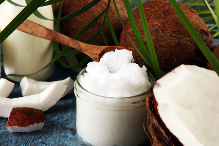 Coconut oil with fresh nut and palm leaves on background. Ripe coconut fruits