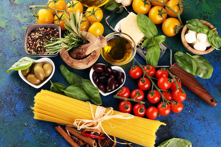 Italian food background with herbs and spices, vine tomatoes, basil, spaghetti, olives, parmesan, olive oil, garlic, peppercorns and rosemaryの写真素材
