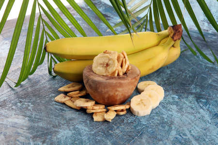 Homemade Dehydrated Banana Chips in a Bowl and fresh banana and slices on tableの写真素材