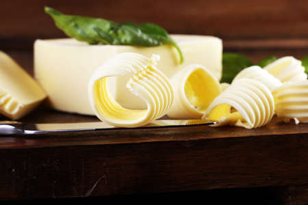 yellow block of fresh butter sliced on wooden cutting board and butter swirls. Slices of margarine or spread, fatty natural dairy product. High-calorie food for cookingの写真素材