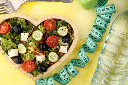 Authentic fresh salad in a wooden heart shaped cup with dumbbells excercise equipment, measuring tape on table. healthy lifestyles, good health Concept with fresh ingredientsの写真素材