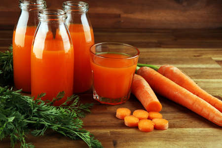 Fresh carrot juice in bottles with organic carrots on rustic tableの写真素材