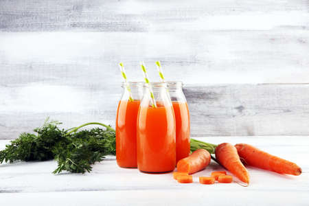 Fresh carrot juice in bottles with organic carrots on rustic tableの写真素材