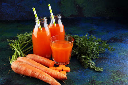 Fresh carrot juice in bottles with organic carrots on rustic tableの写真素材