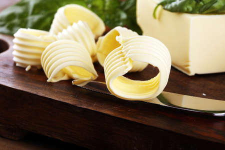 yellow block of fresh butter sliced on wooden cutting board and butter swirls. Slices of margarine or spread, fatty natural dairy product. High-calorie food for cookingの写真素材