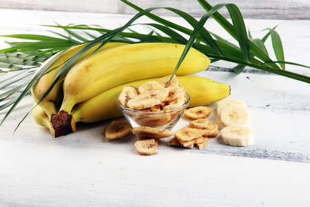 Homemade Dehydrated Banana Chips in a Bowl and fresh banana and slices on tableの写真素材