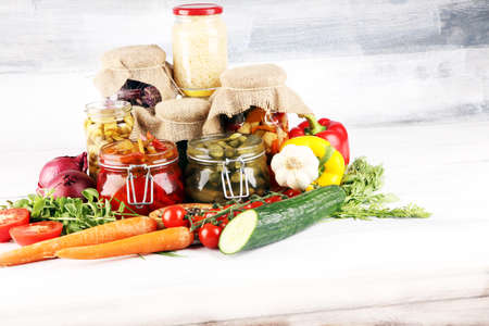 Preserves vegetables in glass jars. Pickled Cucumber, carrot, fermented cabbage and onions on rustic tableの写真素材