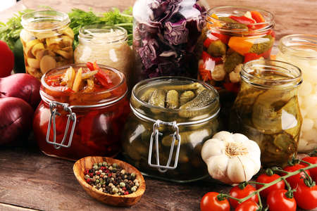 Preserves vegetables in glass jars. Pickled Cucumber, carrot, fermented cabbage and onions on rustic tableの写真素材