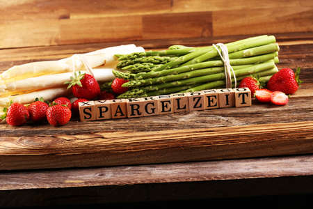 Healthy fresh White and green asparagus and strawberries on vintage background with the german word Spargelzeit in wooden letter. の写真素材