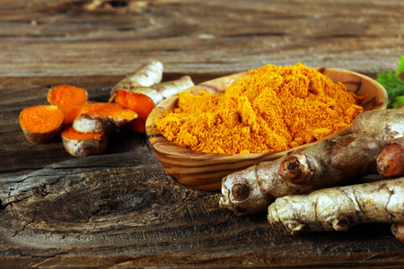 Turmeric powder and fresh turmeric on rustic background.