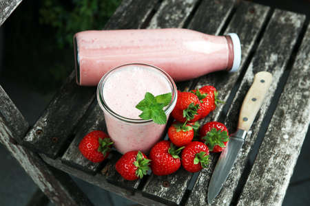 Glass of fresh strawberry shake, smoothie or milkshake and fresh strawberries on table. Healthy food and drink concept with juicy fruitsの写真素材