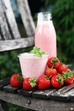Glass of fresh strawberry shake, smoothie or milkshake and fresh strawberries on table. Healthy food and drink concept with juicy fruitsの写真素材