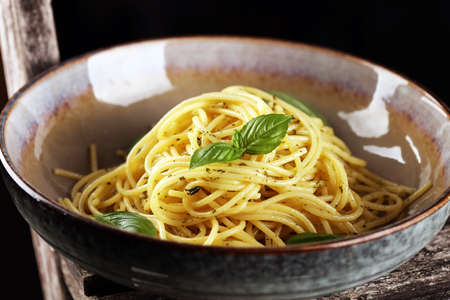 Plate of delicious spaghetti pesto garnished with parmesan cheese and basil on rustic backgroundの写真素材