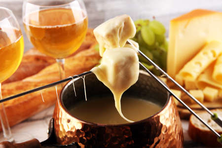 Gourmet Swiss fondue dinner on a winter evening with assorted cheeses on a board alongside a heated pot of cheese fondue with forks dipping breadの写真素材