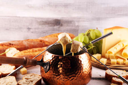 Gourmet Swiss fondue dinner on a winter evening with assorted cheeses on a board alongside a heated pot of cheese fondue with forks dipping breadの写真素材