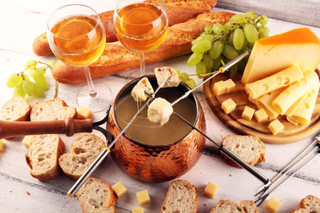 Gourmet Swiss fondue dinner on a winter evening with assorted cheeses on a board alongside a heated pot of cheese fondue with forks dipping breadの写真素材