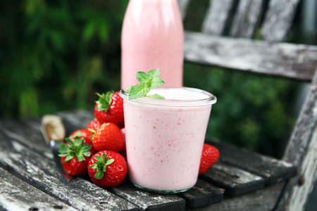 Glass of fresh strawberry shake, smoothie or milkshake and fresh strawberries on table. Healthy food and drink concept with juicy fruitsの写真素材