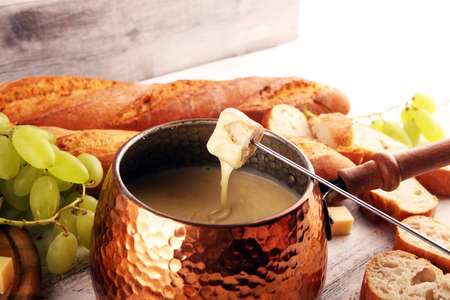 Gourmet Swiss fondue dinner on a winter evening with assorted cheeses on a board alongside a heated pot of cheese fondue with forks dipping breadの写真素材