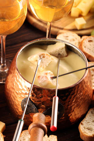Gourmet Swiss fondue dinner on a winter evening with assorted cheeses on a board alongside a heated pot of cheese fondue with forks dipping breadの写真素材