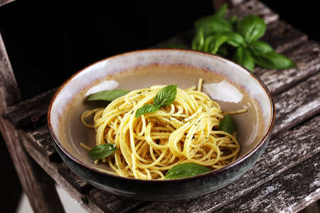 Plate of delicious spaghetti pesto garnished with parmesan cheese and basil on rustic backgroundの写真素材