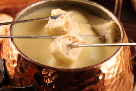 Gourmet Swiss fondue dinner on a winter evening with assorted cheeses on a board alongside a heated pot of cheese fondue with forks dipping breadの写真素材