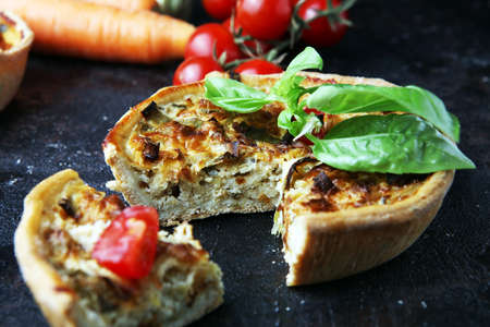 Savory mini quiches or tarts on a rustic board. Flaky dough pies. Fresh basil and tomatoes on handmade quicheの写真素材