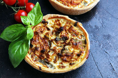 Savory mini quiches or tarts on a rustic board. Flaky dough pies. Fresh basil and tomatoes on handmade quicheの写真素材