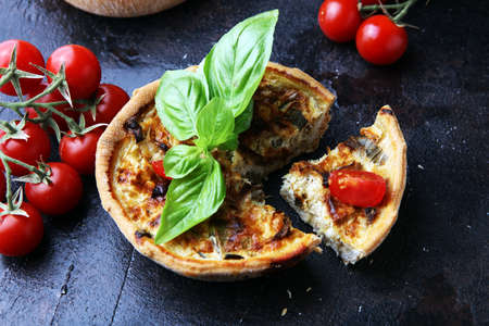 Savory mini quiches or tarts on a rustic board. Flaky dough pies. Fresh basil and tomatoes on handmade quicheの写真素材