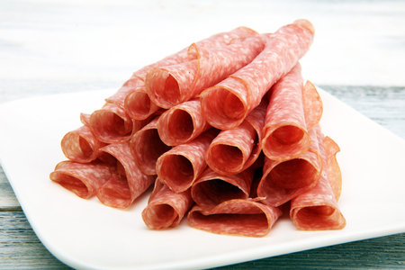 thinly sliced salami. delicious snack rustic salami on wooden white backgroundの写真素材